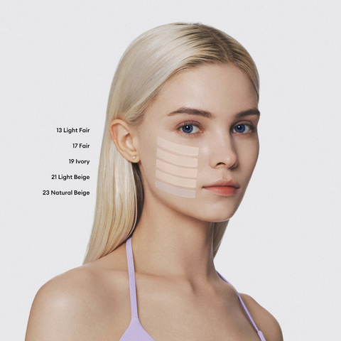 A young woman with pale skin and blonde hair looks at the camera. Swatches of five different foundation shades are visible on her cheek. A young woman with pale skin and blonde hair looks at the camera. Swatches of five different foundation shades are visible on her cheek.