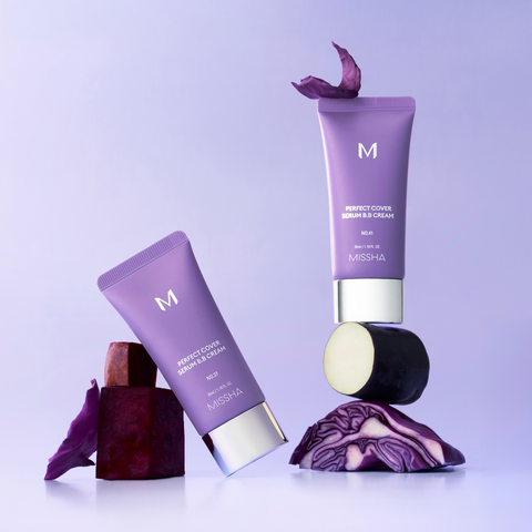 Two tubes of Missha Perfect Cover Serum BB Cream in purple packaging, one upright on an eggplant slice and purple cabbage, the other leaning on brown blocks.
 Two tubes of Missha Perfect Cover Serum BB Cream in purple packaging, one upright on an eggplant slice and purple cabbage, the other leaning on brown blocks.