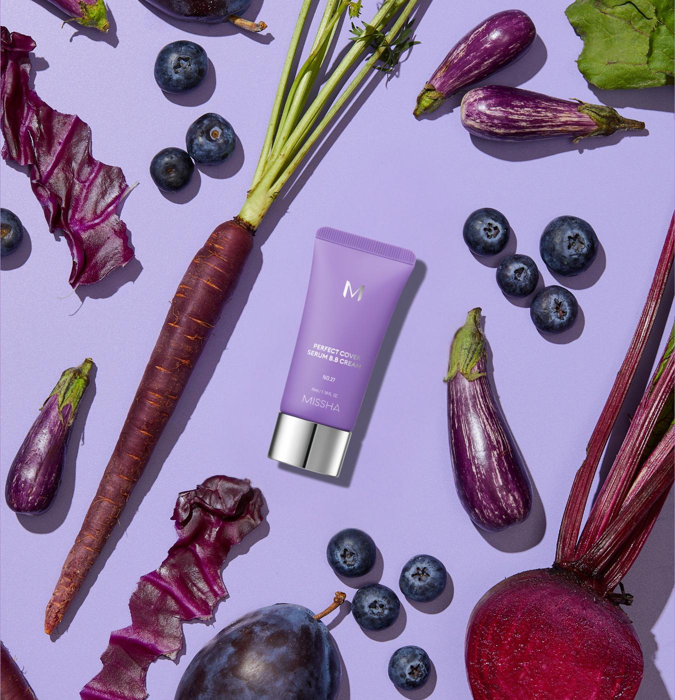 A Missha BB cream tube on a light purple background with purple carrots, blueberries, purple-striped eggplants, a beet, and a plum. A Missha BB cream tube on a light purple background with purple carrots, blueberries, purple-striped eggplants, a beet, and a plum.