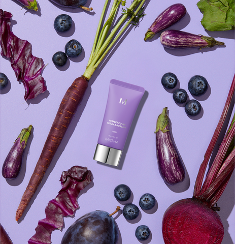 A Missha BB cream tube on a light purple background with purple carrots, blueberries, purple-striped eggplants, a beet, and a plum. A Missha BB cream tube on a light purple background with purple carrots, blueberries, purple-striped eggplants, a beet, and a plum.