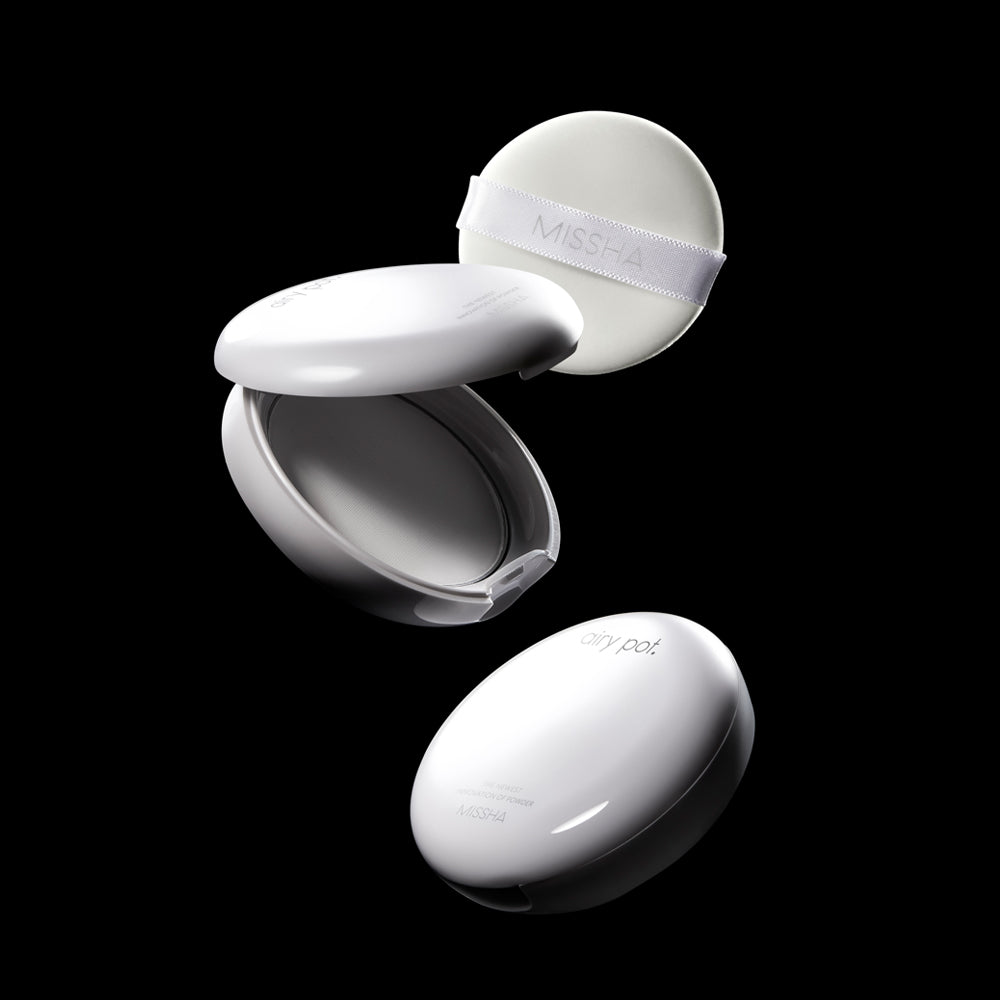 A dynamic shot of two Missha Airy Pot Pressed Powder Pact compacts and a soft white puff applicator against a black background. One compact is closed, and the other is open, displaying the interior and the MISSHA-branded powder puff, highlighting the K-beauty finishing powder and its packaging components. A dynamic shot of two Missha Airy Pot Pressed Powder Pact compacts and a soft white puff applicator against a black background. One compact is closed, and the other is open, displaying the interior and the MISSHA-branded powder puff, highlighting the K-beauty finishing powder and its packaging components.