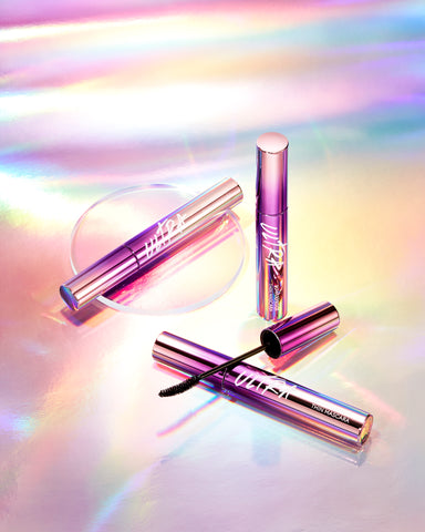 A tube of MISSHA Ultra Powerproof Thin Mascara with a brush, displayed on a reflective surface with a colorful, holographic background. A tube of MISSHA Ultra Powerproof Thin Mascara with a brush, displayed on a reflective surface with a colorful, holographic background.