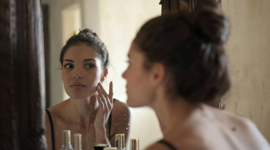 Woman Looking in Mirror with Skincare Products