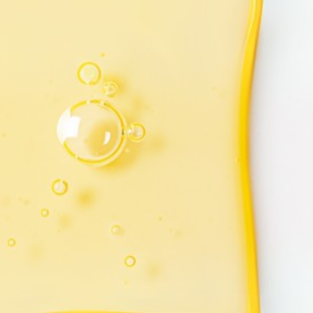 Close-up of a bright yellow serum texture with air bubbles, showing a glossy, smooth consistency and radiant finish.