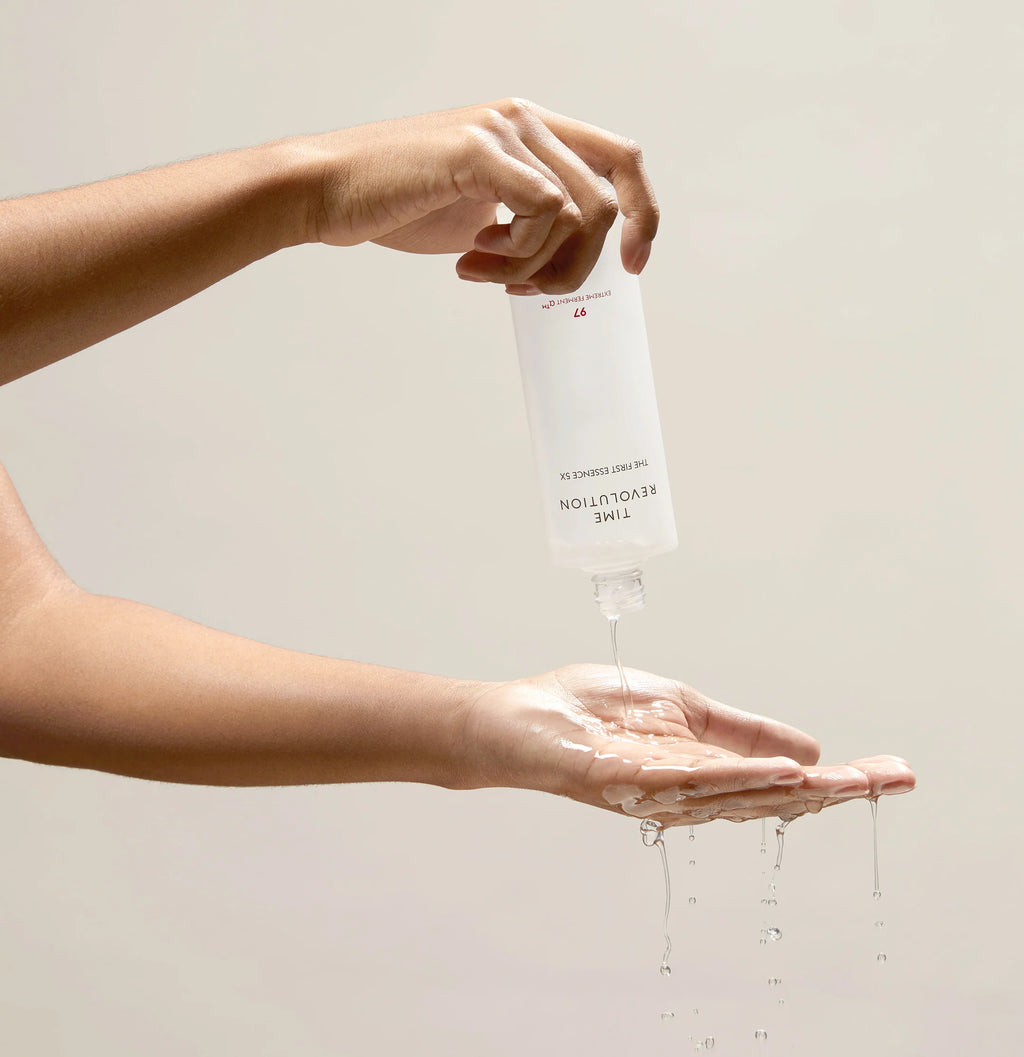 Hands pouring MISSHA Time Revolution The First Essence onto the palm, with clear, watery liquid dripping naturally, showcasing the lightweight and hydrating texture of the essence.