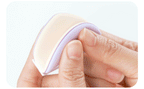 Close-up shot of a hand gently squeezing the soft, thick material of the tear-drop shaped Missha Layering Puff. The puff is beige on one side and light purple on the other, demonstrating its dual-layer structure and flexibility for applying cushion foundation.