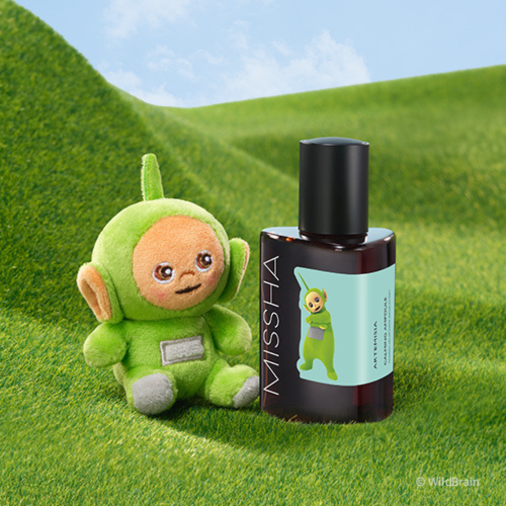 MISSHA Artemisia Calming Ampoule featuring a Teletubbies character on the label, displayed on green grass beside a matching Teletubbies plush toy under a blue sky.