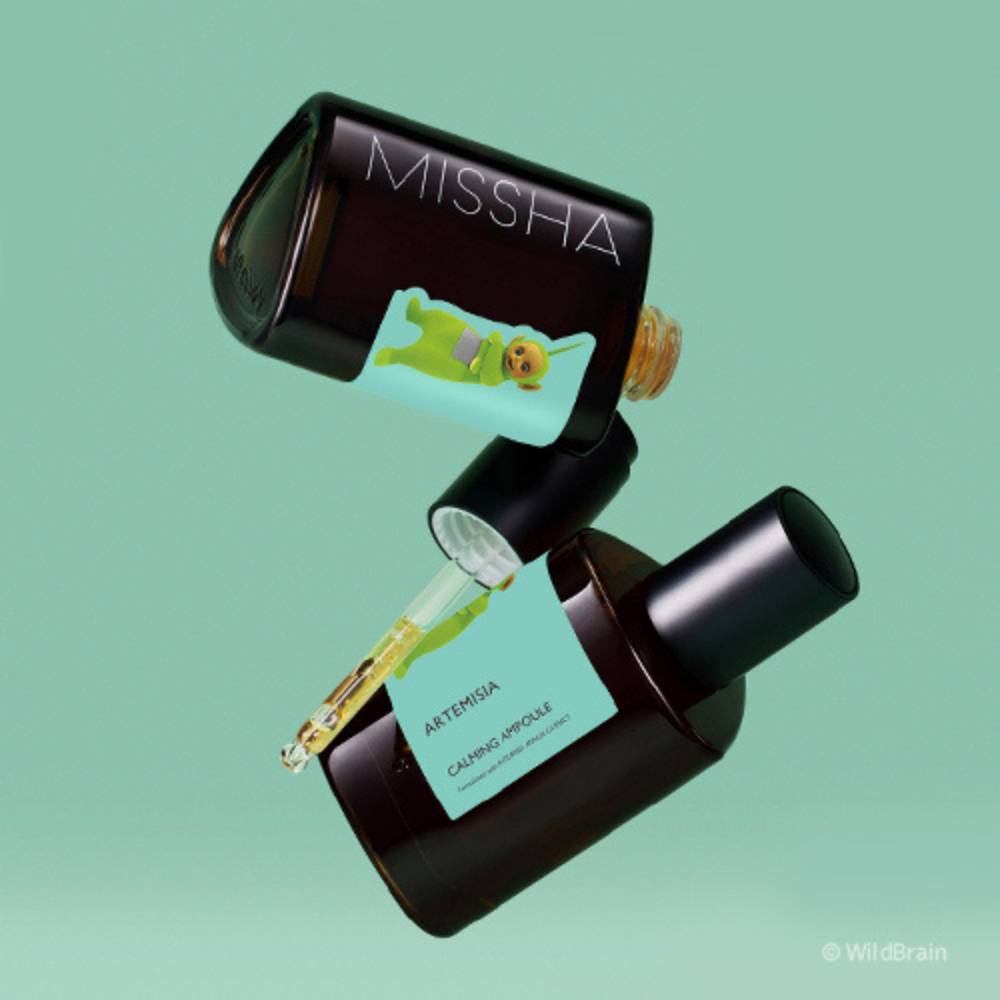 Two brown glass ampoules of MISSHA Artemisia Calming Ampoule floating against a mint green background, featuring a Teletubbies character illustration on the label.
