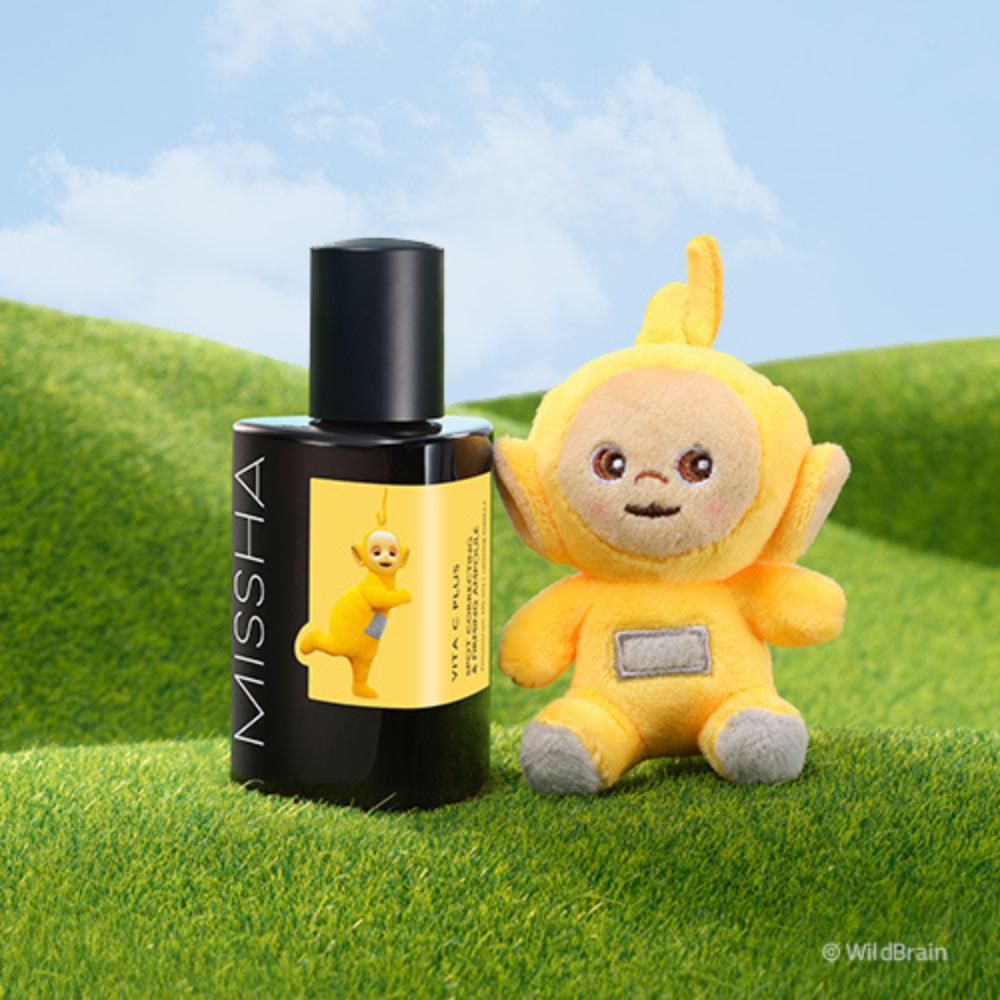 MISSHA Vita C Plus Spot Correcting Ampoule featuring a Teletubbies character on the label, displayed on green grass beside a matching yellow Teletubbies plush toy under a blue sky.