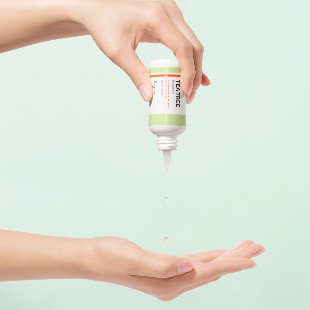 Hand holding a bottle of tea tree oil over another hand on a light green background
