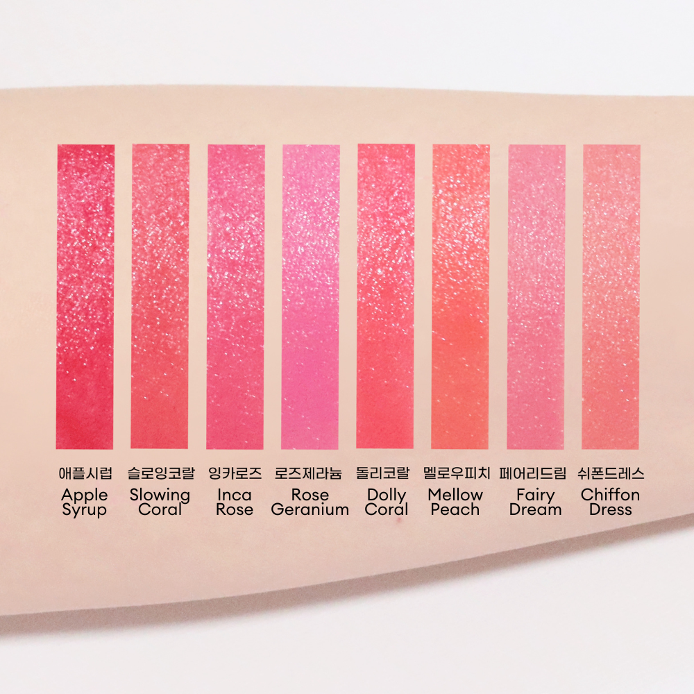 Swatches of eight glossy lip shades applied on skin, ranging from deep red to coral and pink tones. The shades from left to right are Apple Syrup, Slowing Coral, Inca Rose, Rose Geranium, Dolly Coral, Mellow Peach, Fairy Dream, and Chiffon Dress.