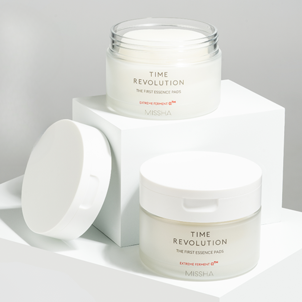 MISSHA Time Revolution The First Essence Pads in sleek frosted jars with white lids, displayed on minimalist white blocks for a clean and modern aesthetic.