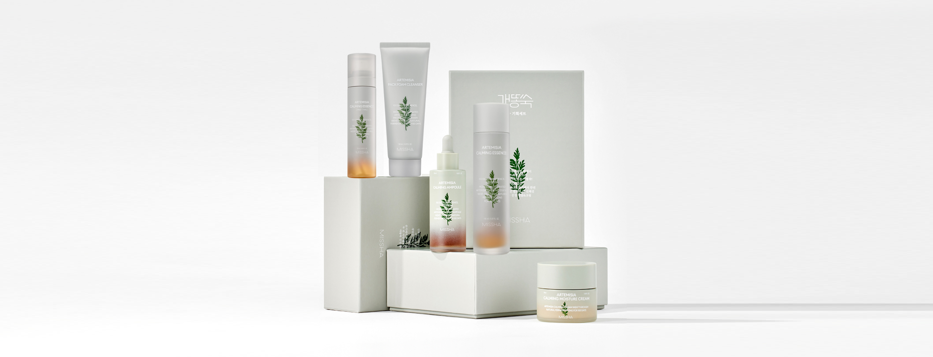 Skincare collection with calming essence, foam cleanser, ampoule, and moisturizer, elegantly arranged on white boxes.