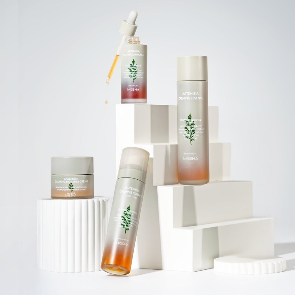MISSHA Artemisia Calming skincare line displayed on white geometric blocks, featuring the Calming Essence, Calming Ampoule, Calming Moisture Cream, and Calming Essence Mist. The packaging is minimalist with frosted glass and herb illustrations, emphasizing a soothing and natural aesthetic.