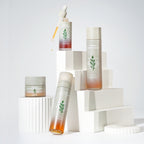 MISSHA Artemisia Calming skincare line displayed on white geometric blocks, featuring the Calming Essence, Calming Ampoule, Calming Moisture Cream, and Calming Essence Mist. The packaging is minimalist with frosted glass and herb illustrations, emphasizing a soothing and natural aesthetic.
