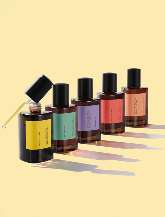 Five elegant bottles of skincare oils in varying colors, a dropper applying from the black bottle.
