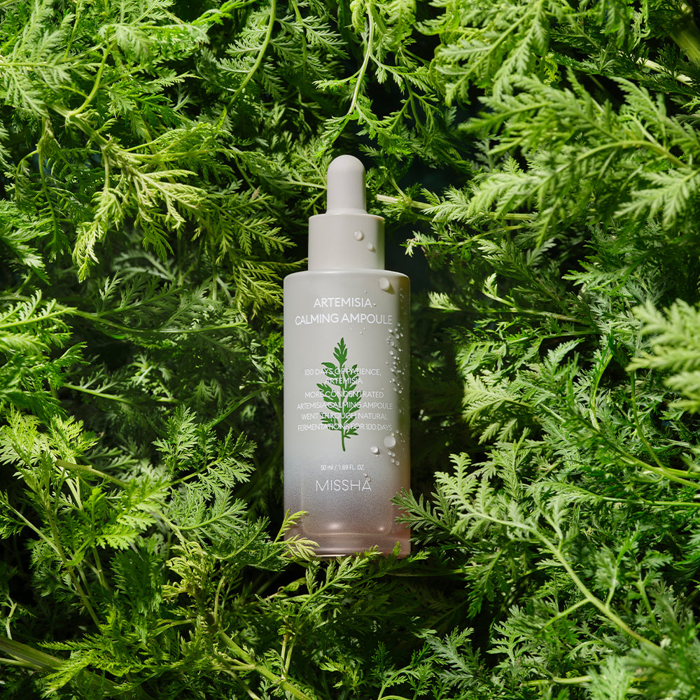 MISSHA Artemisia Calming Ampoule bottle placed among lush green Artemisia leaves, highlighting its natural, soothing ingredients and calming skincare benefits.