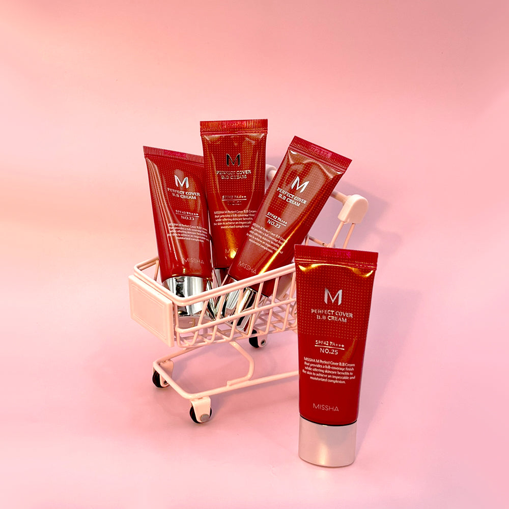 Five tubes of MISSHA M Perfect Cover BB Cream arranged in a miniature shopping cart on a soft pink background.