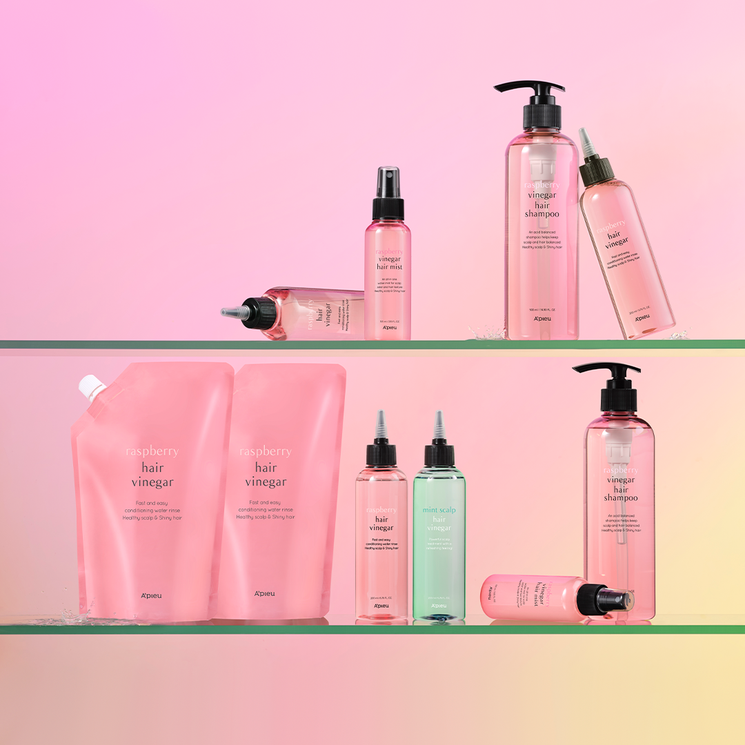 A’PIEU Raspberry Hair Vinegar and Mint Scalp Hair Vinegar collection displayed on glass shelves, featuring shampoos, mists, refill pouches, and scalp treatments in pink and mint packaging for shiny, healthy hair.