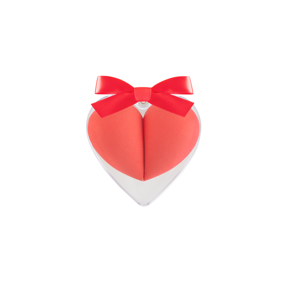 A heart-shaped sponge blender with a coral pink color and a red bow on the top