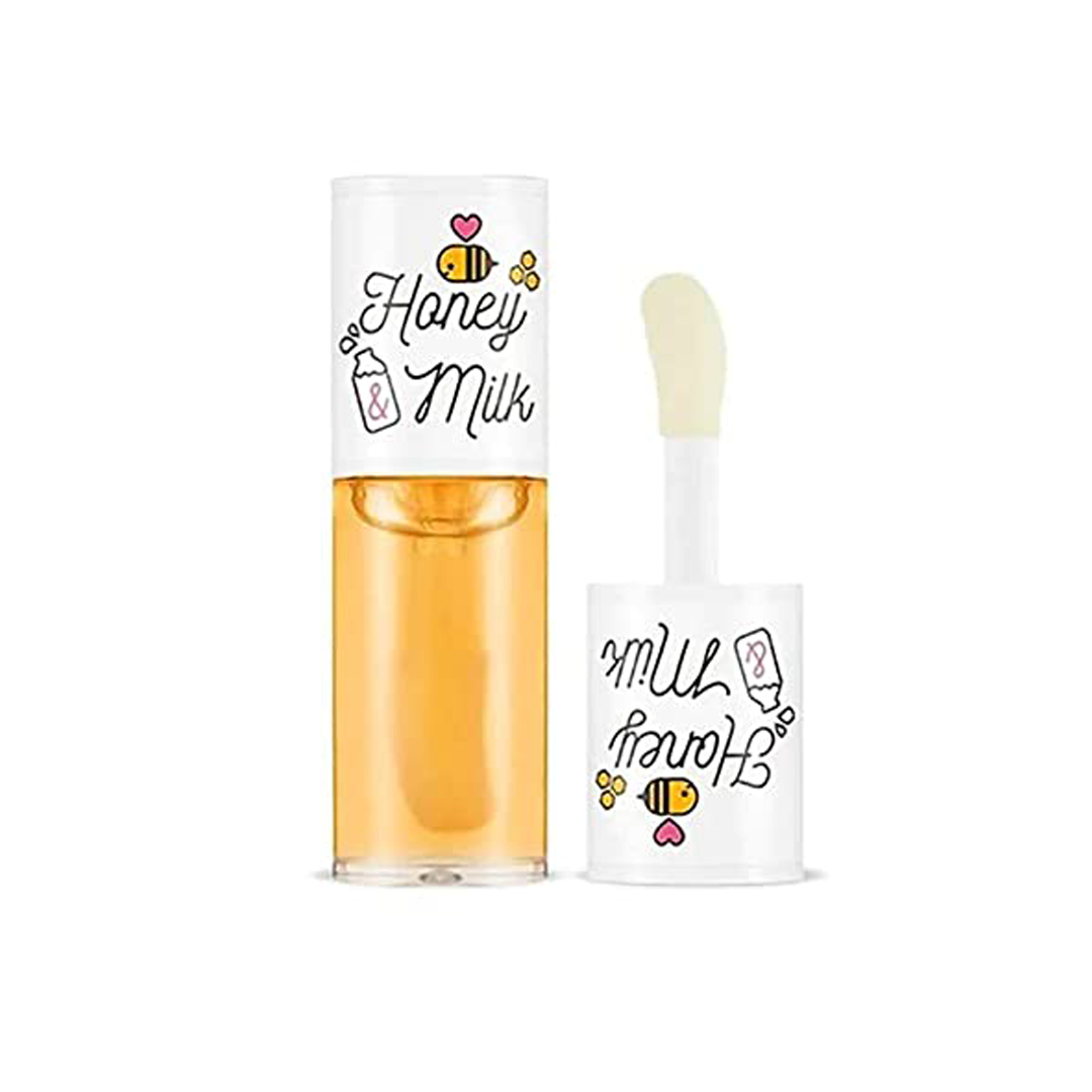 A'pieu Honey & Milk Lip Oil in a clear tube with orange-colored product visible inside. The packaging is adorned with illustrations of honeycomb and the product is equipped with a white applicator.