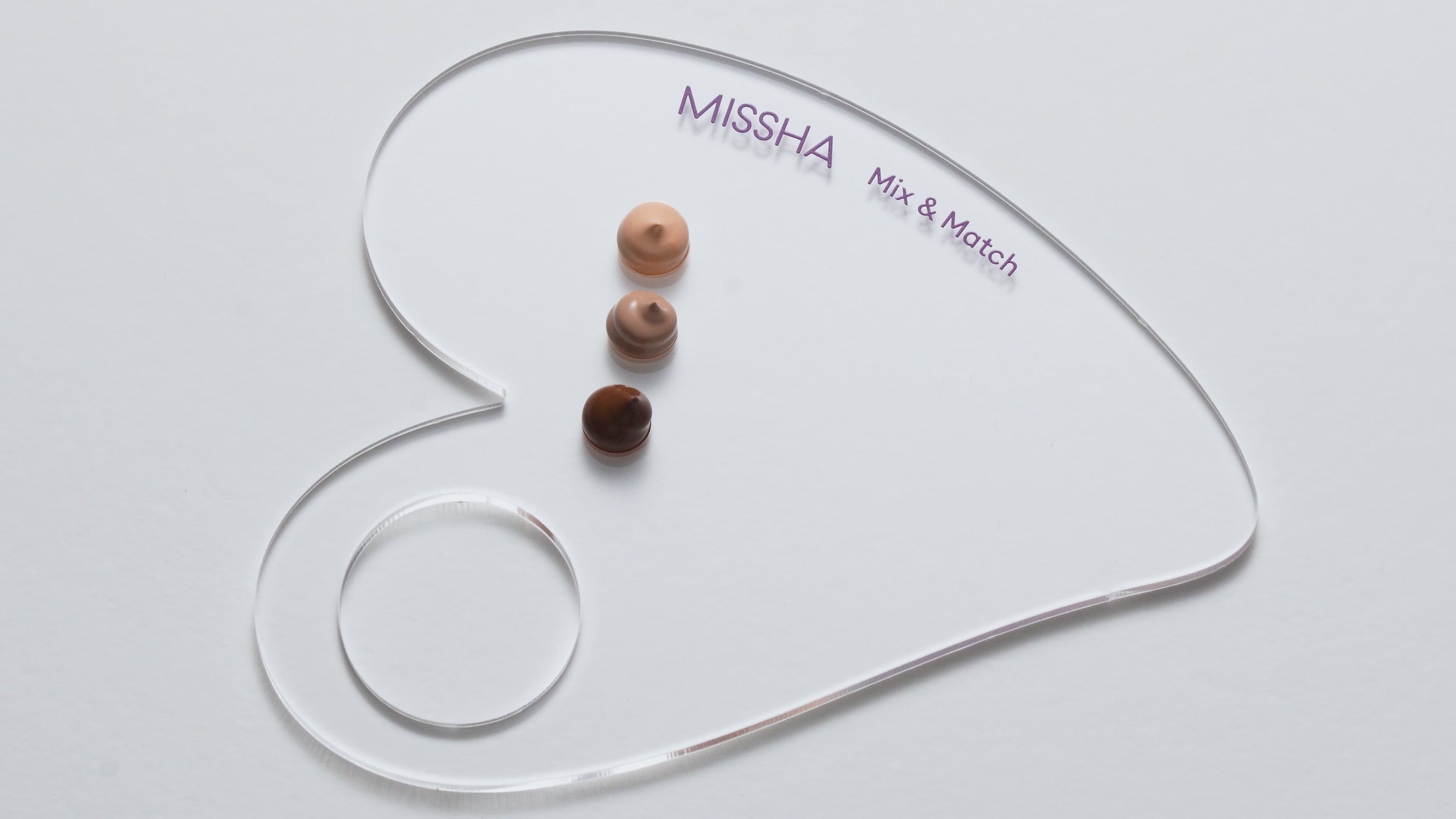 Transparent heart-shaped MISSHA Mix & Match palette with three foundation shades in varying tones dotted on its surface against a white background.