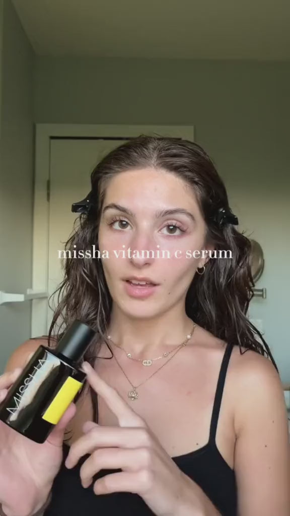 Person holding a MISSHA Vita C Plus Serum bottle with a yellow label, demonstrating the product in a minimal indoor setting with text overlay that reads “MISSHA vitamin c serum.”