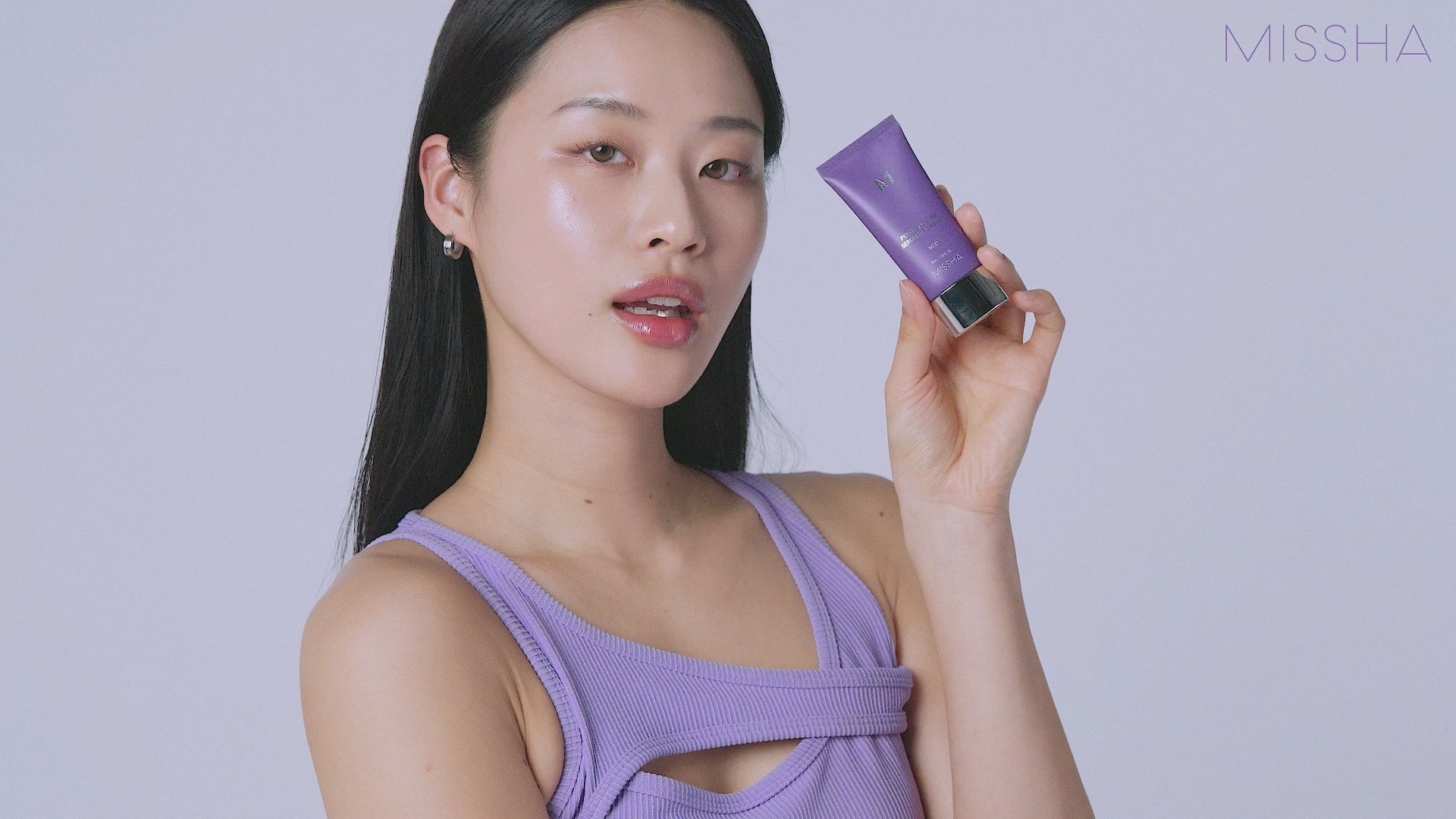 Person wearing a lavender top holding a tube of MISSHA Perfect Cover Serum BB Cream in matching lavender packaging, posing against a light purple background with the MISSHA logo.