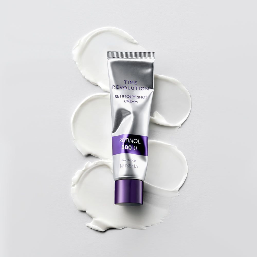 MISSHA Time Revolution Retinol 500 Shot Cream tube placed flat on a white surface with smooth cream swatches beneath it, showcasing its silky texture and elegant silver-purple packaging.