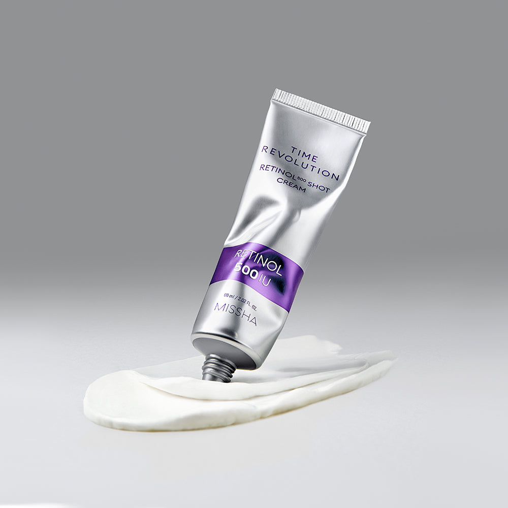 MISSHA Time Revolution Retinol 500 Shot Cream tube standing on a smooth smear of white cream, highlighting its rich texture and sleek silver-and-purple packaging against a minimalist gray background.