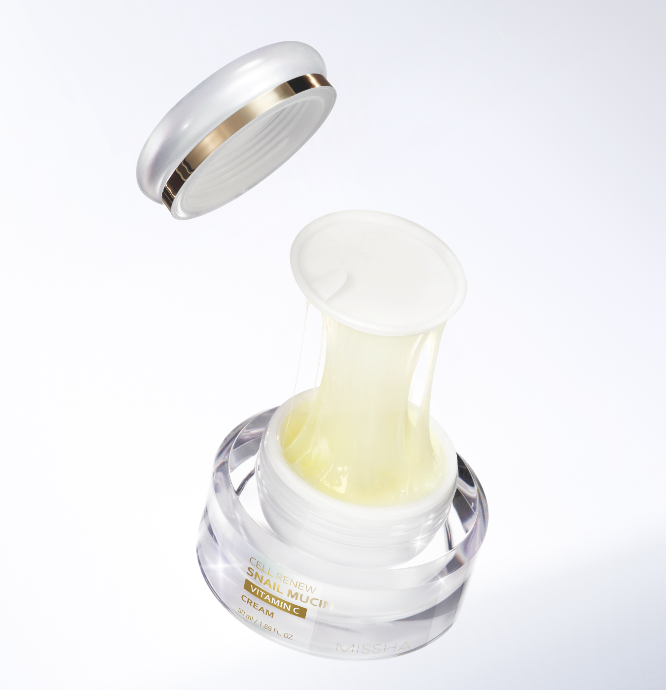Overhead studio shot of the Missha Cell Renew Snail Mucin Vitamin C Cream with the lid removed, showing the golden-hued cream stretching due to the high concentration of snail mucin.