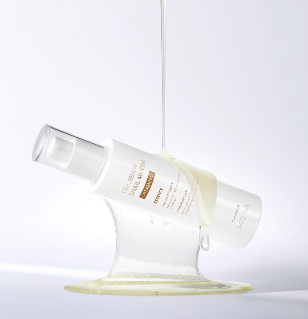 Studio shot of the Missha Cell Renew Snail Mucin Vitamin C Essence bottle tilted, held up by a visible stream of the thick, viscous serum that highlights the snail mucin ingredient's texture for intense skin repair and anti-aging.