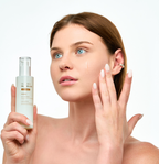 A woman with blue eyes holding the Missha Cell Renew Snail Mucin Vitamin C Essence while gently applying a drop of the product to her cheek, demonstrating the correct way to use this skin-revitalizing serum for a radiant complexion.