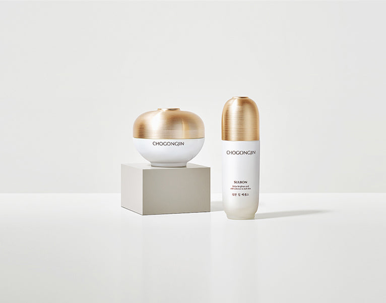 Two skincare products with gold accents on a white backdrop: one sleek bottle and one spherical jar, minimalist style.