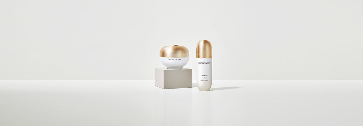 Two skincare products with gold accents on a white backdrop: one sleek bottle and one spherical jar, minimalist style.