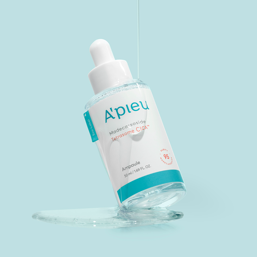 The A'pieu Madecassoside Tetrasome Cica Ampoule bottle is tilted, with serum dripping down and pooling at the base. A stream of the clear, liquid Cica serum pours onto the bottle, showcasing its lightweight, non-greasy texture for sensitive and irritated skin.
