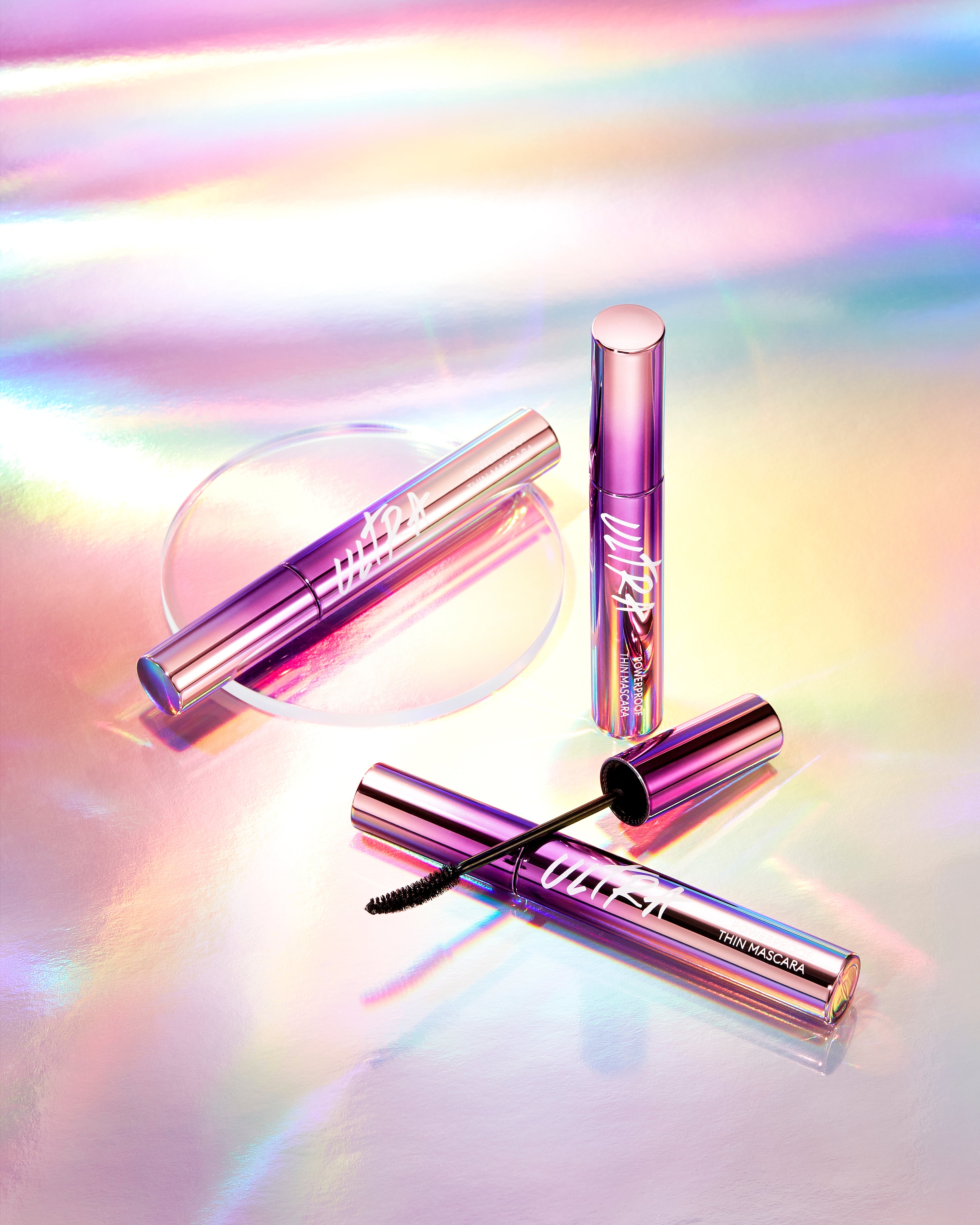 A tube of MISSHA Ultra Powerproof Thin Mascara with a brush, displayed on a reflective surface with a colorful, holographic background.