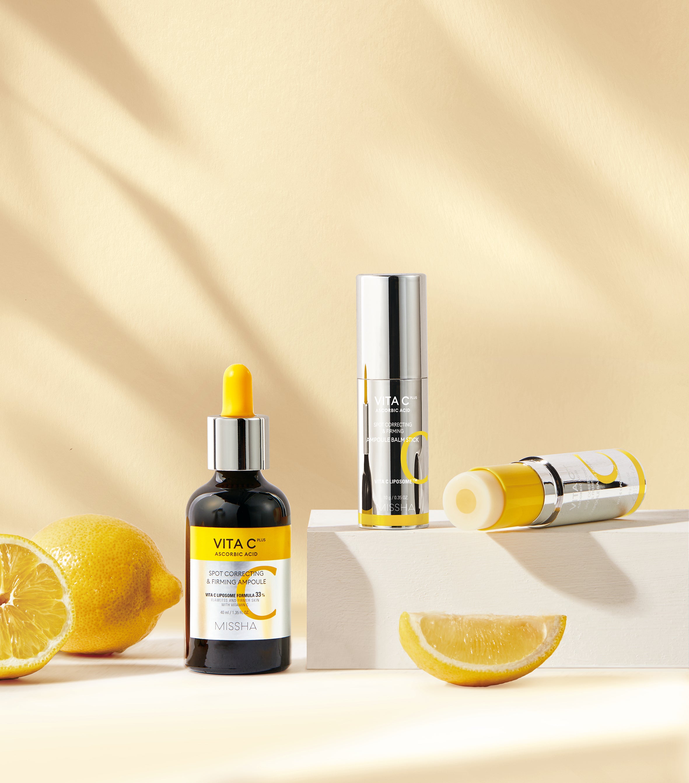 A still-life arrangement featuring the Missha Vita C Plus Spot Correcting & Firming Ampoule dropper bottle and the new Balm Stick alongside cut lemons. This promotes the potent Vitamin C ingredients used to visibly fade dark spots and brighten dull skin.