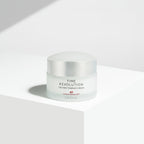A jar of Missha Time Revolution The First Essence Cream placed on a white surface with a shadow falling across the frame.