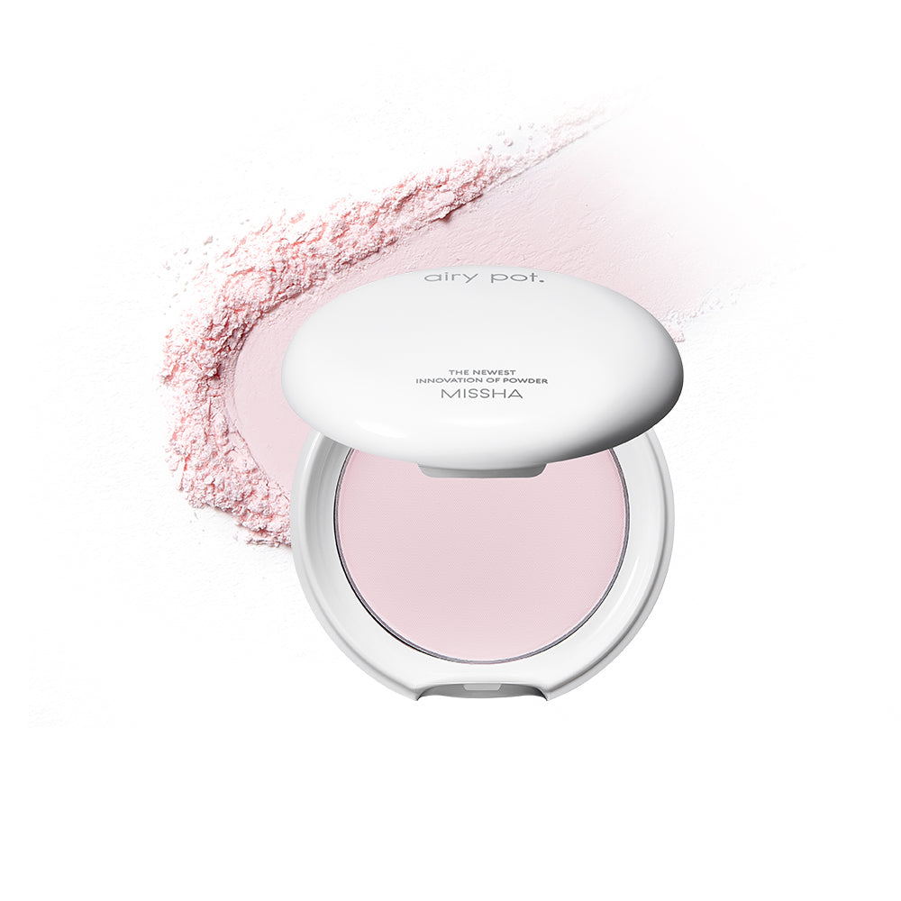 Missha Airy Pot. A compact white powder pact with a pressed powder formula, displayed against a white background. With a light pink trail of powder behind.