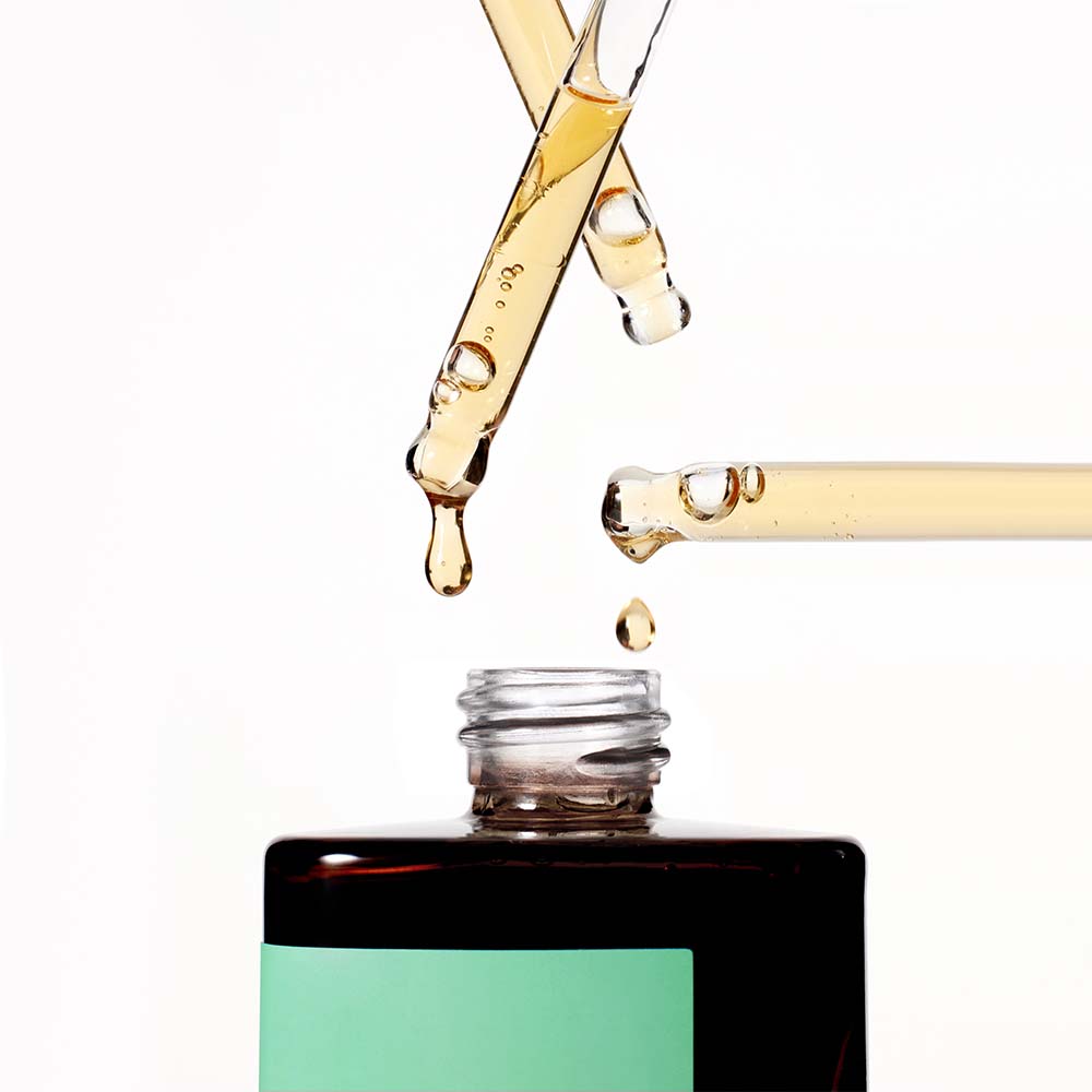 Close-up of multiple droppers dispensing the amber-colored liquid of the Missha Time Revolution Artemisia Calming Ampoule into the bottle opening. This visual emphasizes the potent, soothing serum texture for sensitive skin.