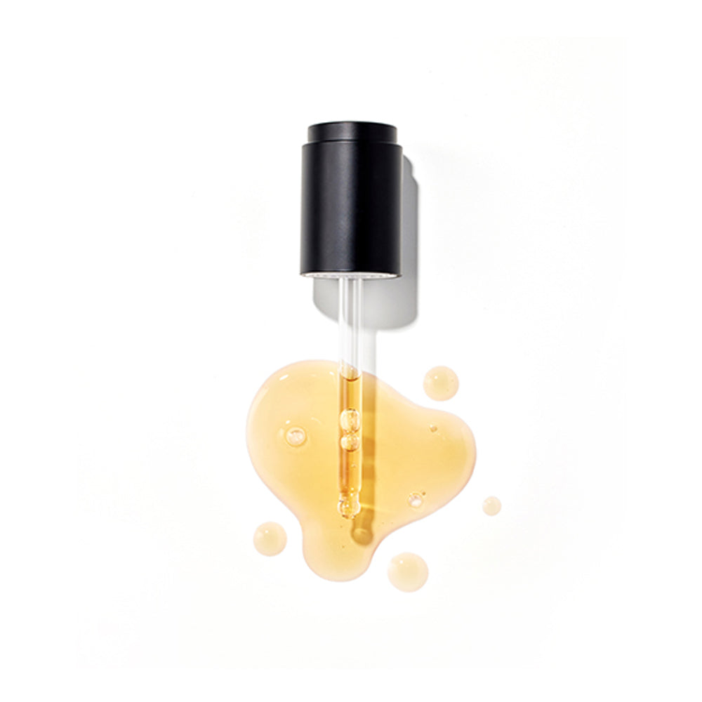 Overhead view of a black-capped dropper resting in a puddle of the golden-yellow Missha Time Revolution Artemisia Calming Ampoule serum. This detail shot emphasizes the concentrated liquid texture of the calming and hydrating product.