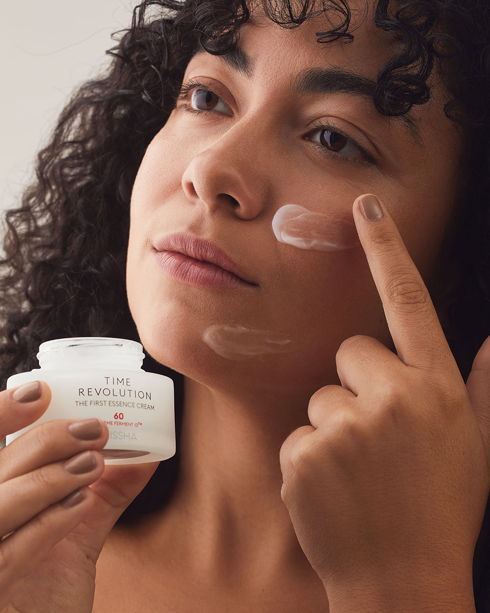 Model applying MISSHA Time Revolution The First Essence Cream 60 to face, showing smooth hydrating texture and brightening skincare effect.
