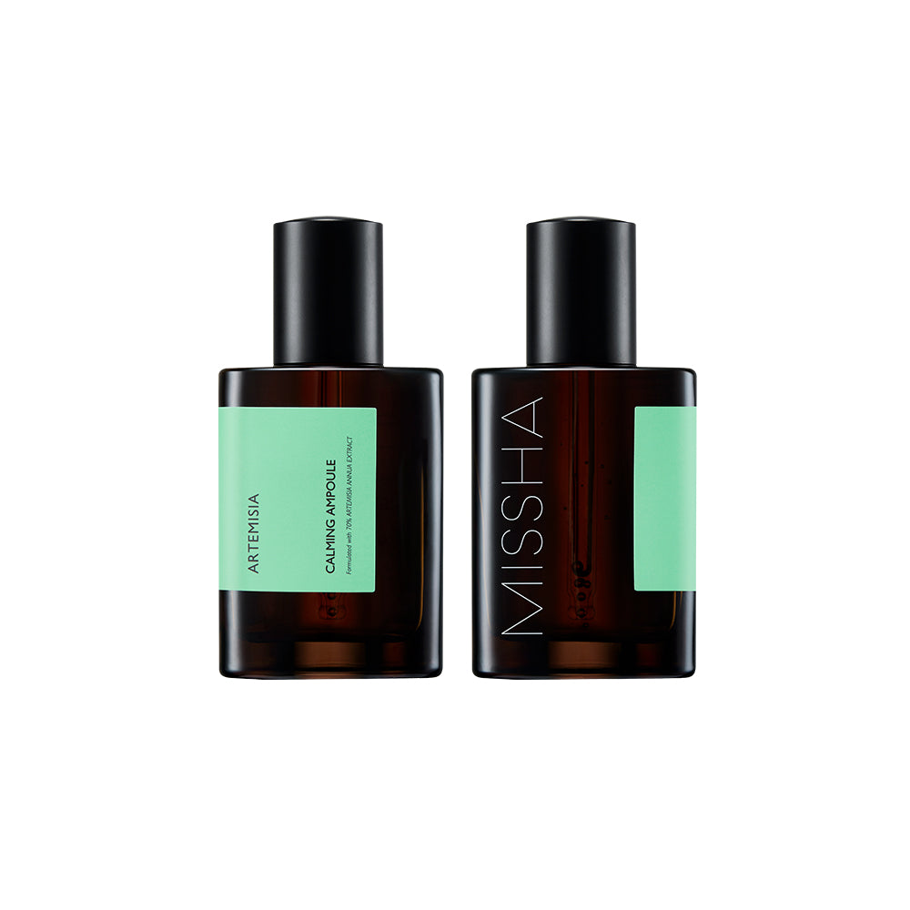 Two dark amber bottles of the Missha Time Revolution Artemisia Calming Ampoule with mint green labels and black caps. This shot shows the front and back of the K-beauty calming ampoule packaging, featuring the Artemisia ingredient.