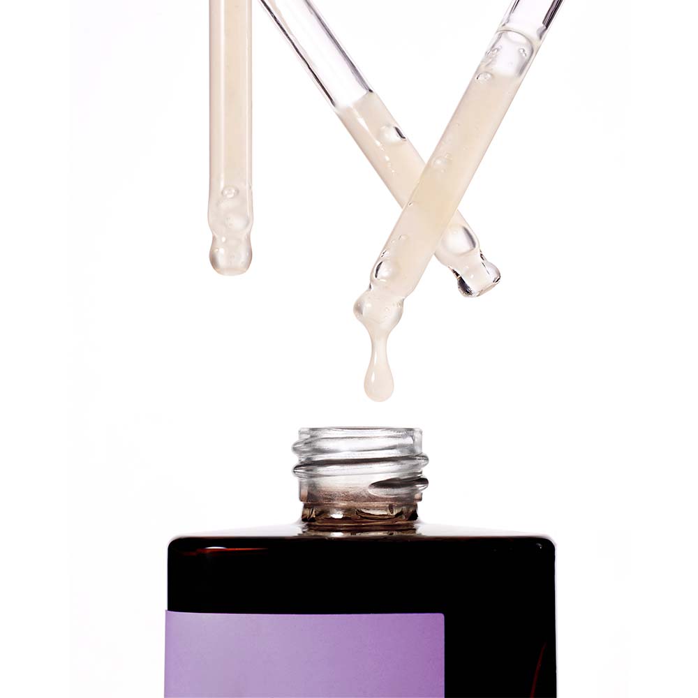 Close-up of multiple droppers dispensing the light, milky, viscous liquid of the Missha Time Revolution Night Repair Ampoule 5X into the bottle opening. This emphasizes the concentrated texture of the anti-aging serum for overnight skin repair.